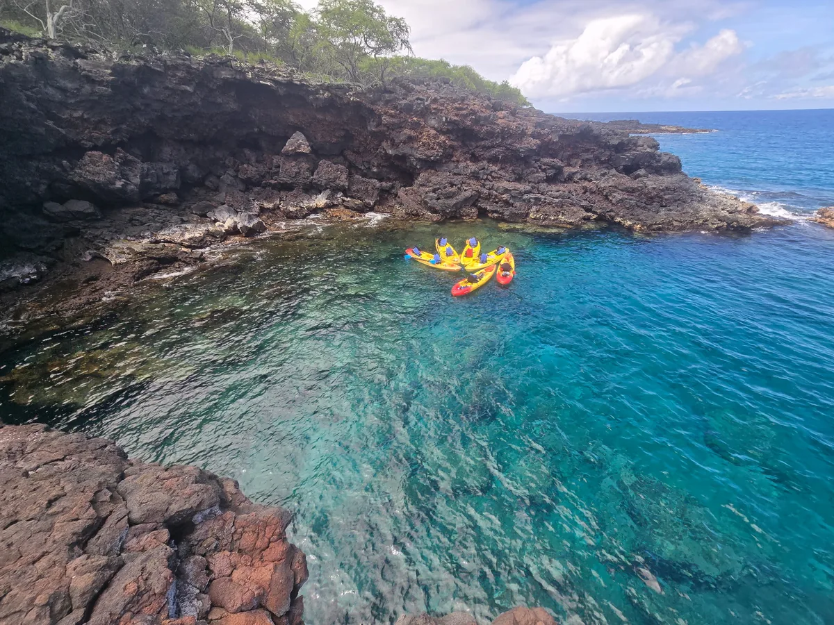 Kayaks in a turquoise cove beneath the lava cliffs, seen from above