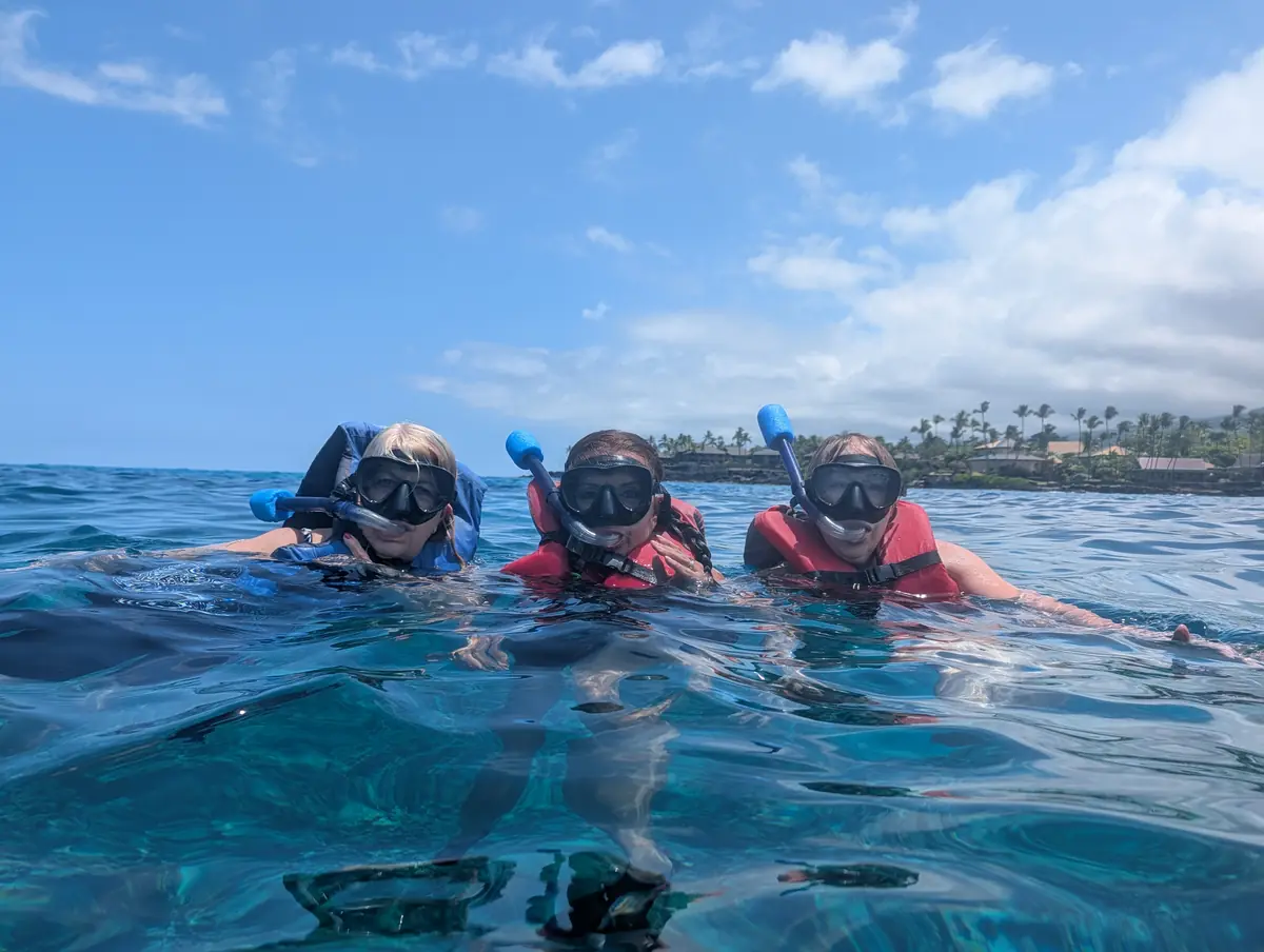 Three guests in red life vests snorkeling off the Kona coast