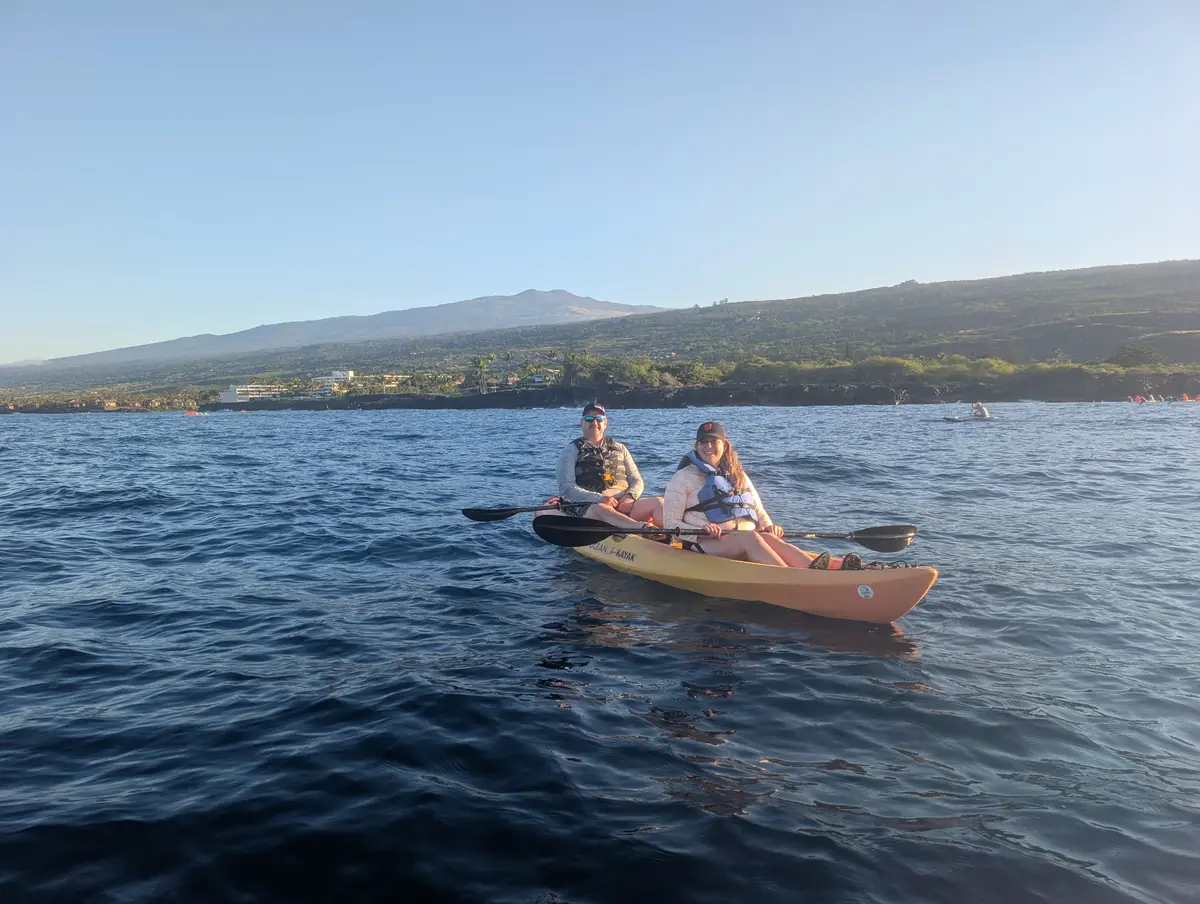 Two guests in a kayak on calm early-morning water, Hualālai behind
