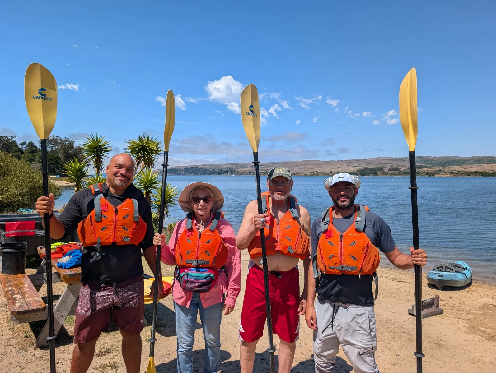 Winfield and three fellow paddlers in life jackets, standing on the beach holding their paddles